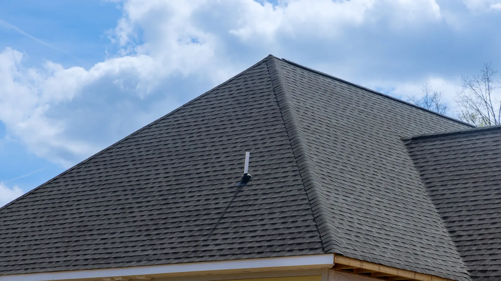 Vent pipe on a dark shingle hip roof beneath a cloudy sky